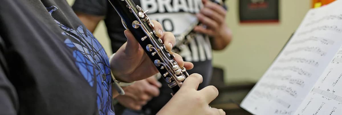 Person spielt Klarinette, im Hintergrund Notenblatt und weitere Musizierende